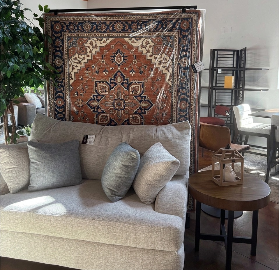 Morgan Creek rug display rack holding a warm patterned area rug directly behind a sofa in a home furnishings showroom